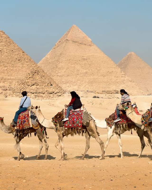 People riding camels past the Giza pyramids
