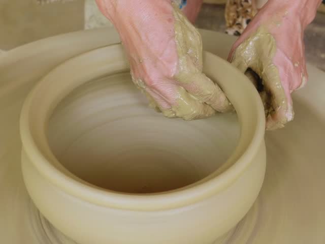 Hands shaping clay on a pottery wheel